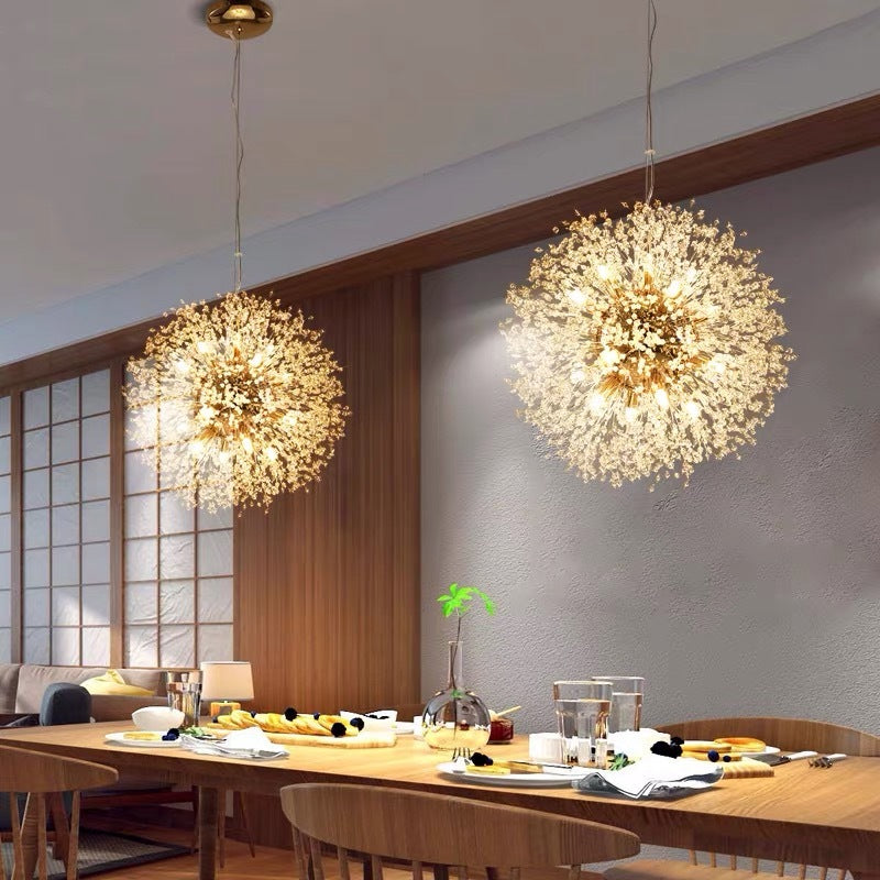 Two gold Lili dandelion lights above wood dining table with place settings and glass vases beside window panels