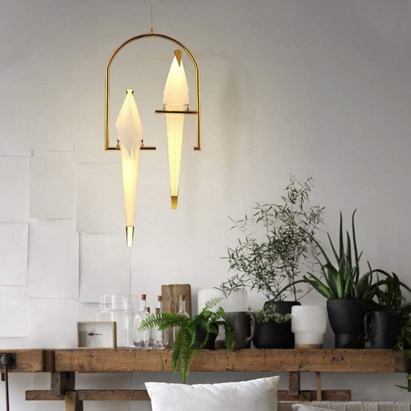 Illuminated two-bird pendant in a light room with plants.