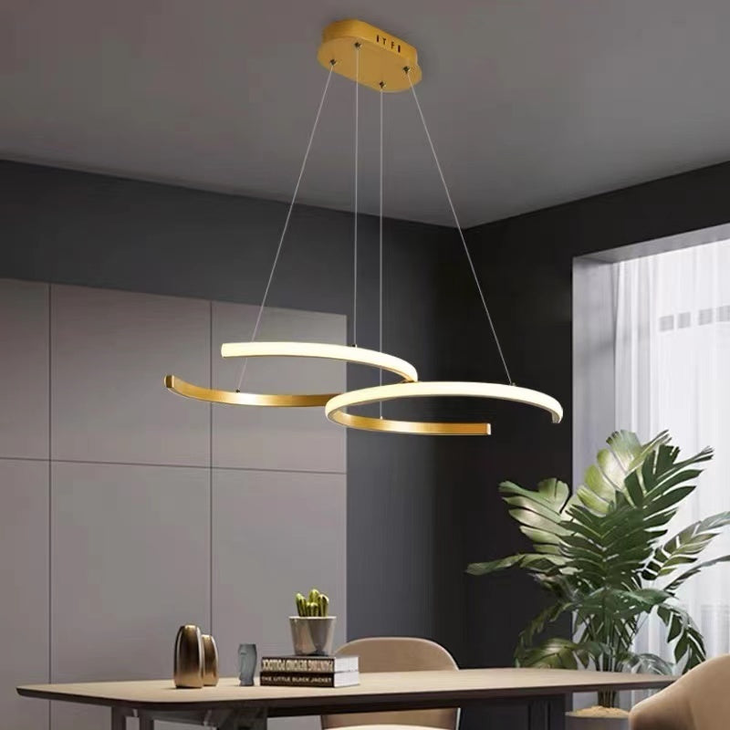 Gold Louise Double-C pendant above a dining table beside a plant.