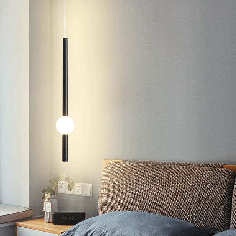 Carr black rod pendant with illuminated white globe beside a bed.