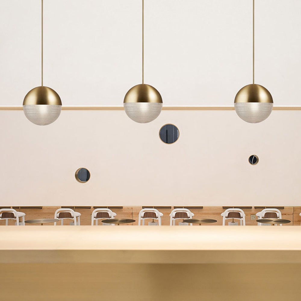 Three Gold globe pendants in a row above a cafe-style counter, with circular wall mirrors, wooden benches and white chairs
