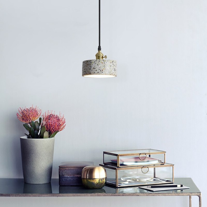 Short speckled drum pendant above a console with a flower vase and glass display boxes
