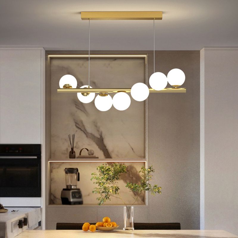 Seven-light Valentina gold globe pendant above a kitchen island, with a marble-patterned wall behind it.