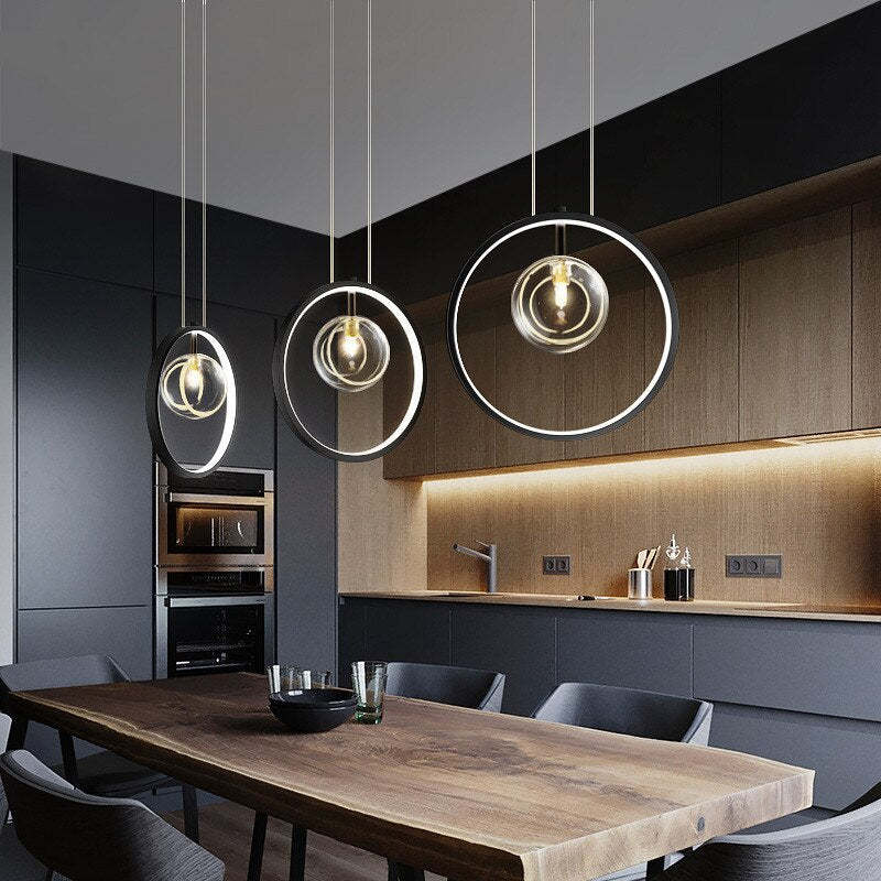 Three separate one-globe ring pendants above a wood dining table beside dark kitchen cabinets