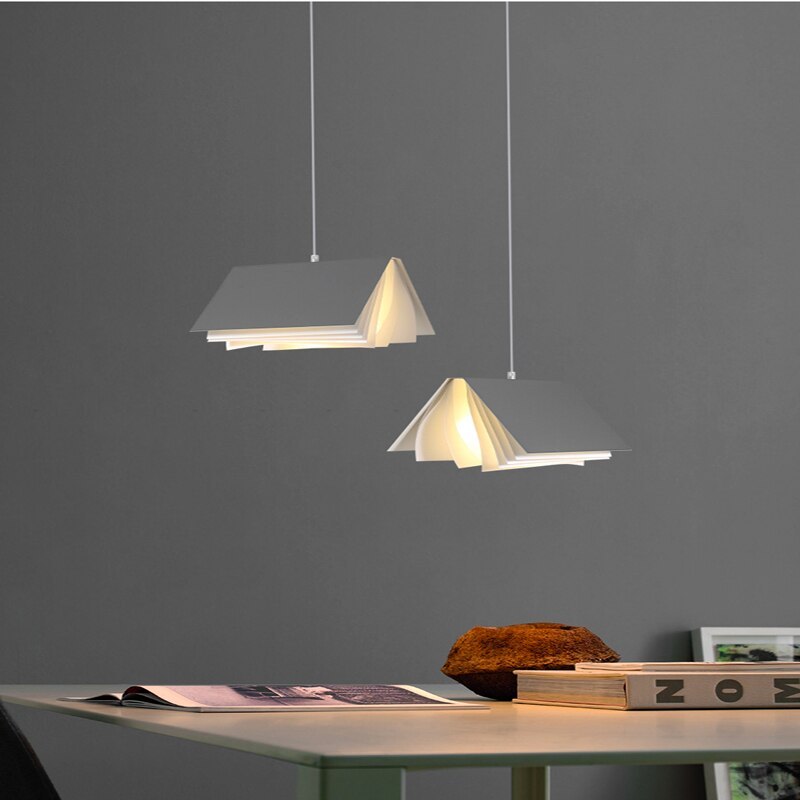 Two separate Gray Sienna book-style pendants above a table with an open printed book, stacked books and a large ornament