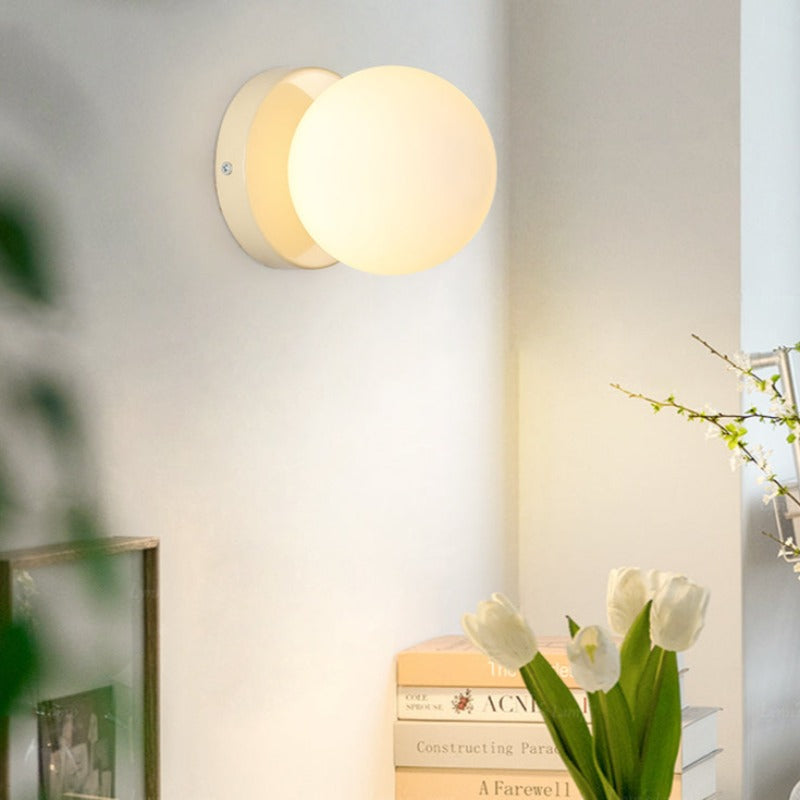 White globe wall sconce lit above flowers and shelf