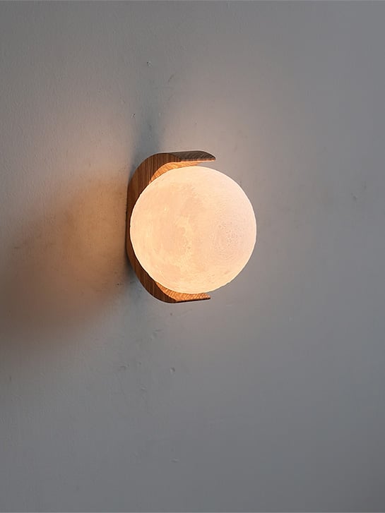 Close angled view of the warm moon-textured globe and crescent wood grain against a plain wall