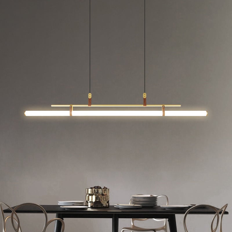 Gold linear pendant above a black dining table with stacked plates and a gold-tone jug against a gray wall
