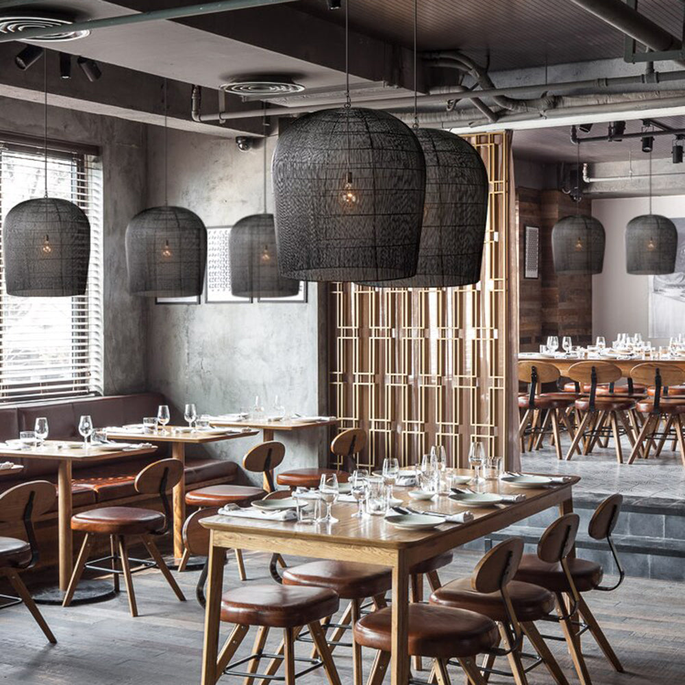 Black woven cage pendants above wooden tables and brown chairs in a restaurant with exposed ceiling services