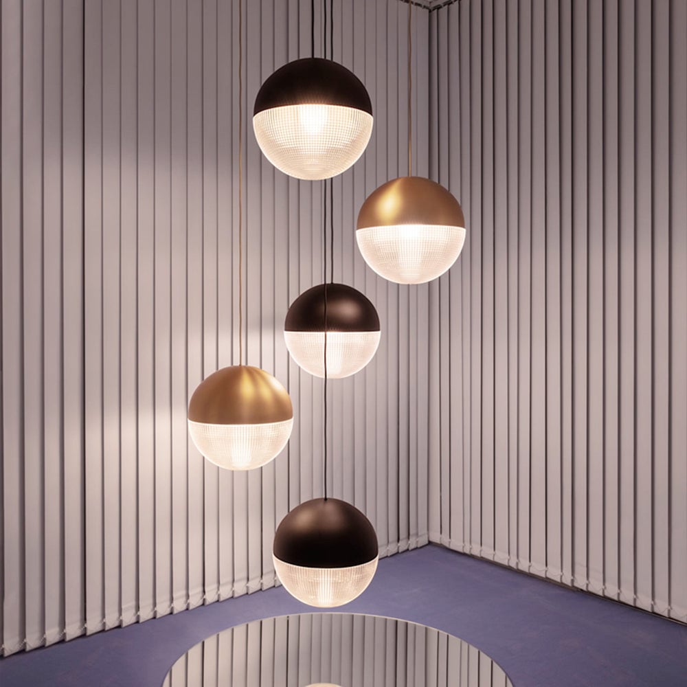 Five separate Black and Gold globe pendants at varied heights in a white slatted corner above a reflective round table
