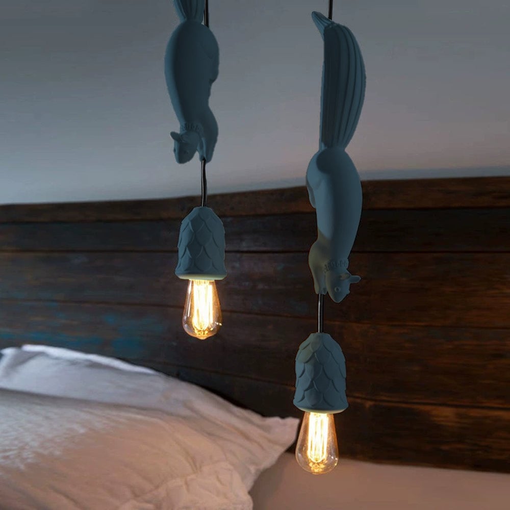 Two blue squirrel pendants beside a bed with a white pillow and dark wooden headboard