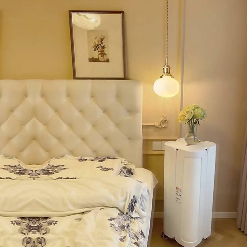 Round Valentina pendant lit above a bedside cabinet beside a tufted headboard