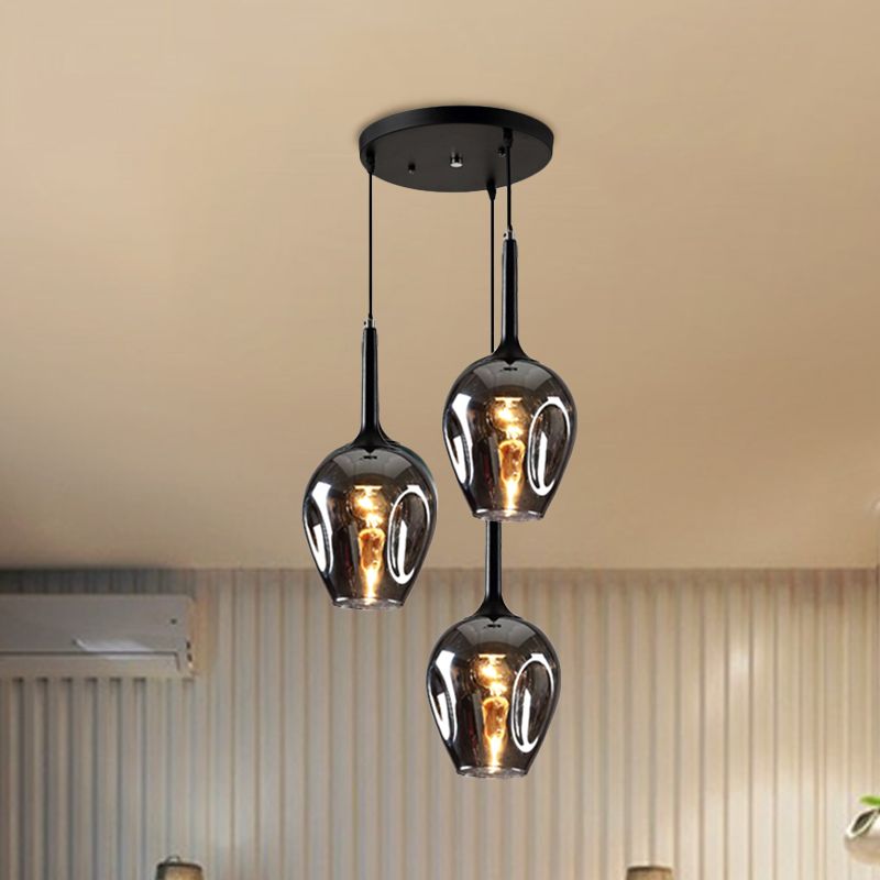 Smoke-gray glass cluster pendant with three lit shades in front of curtains