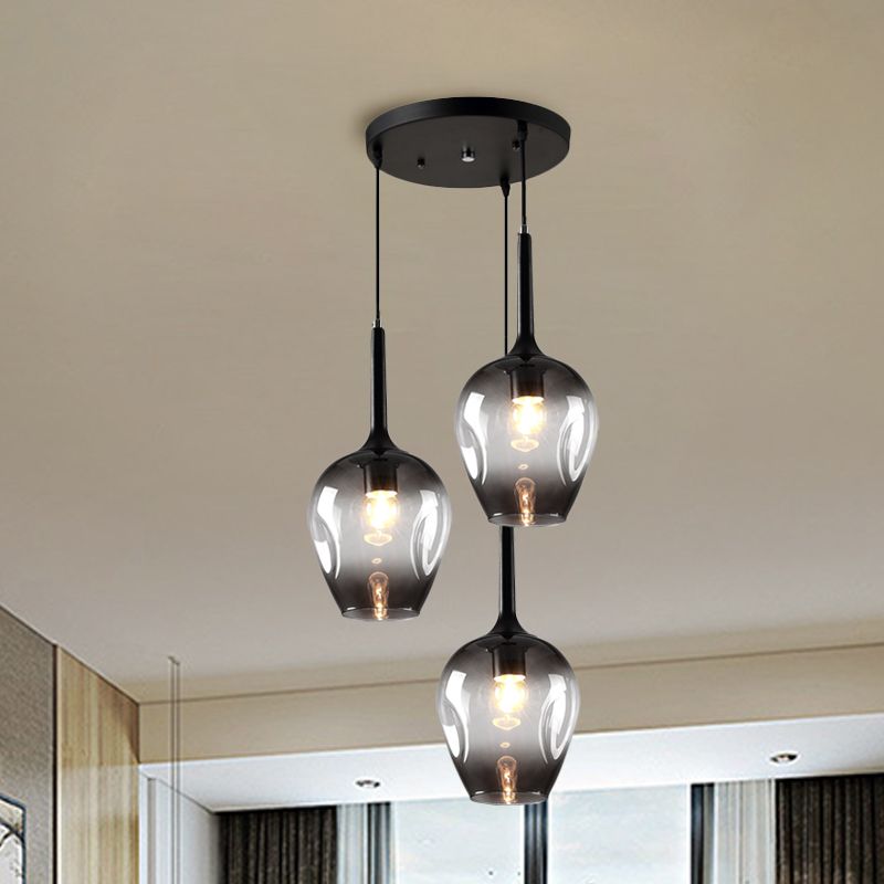 Gray glass cluster pendant with three staggered shades near a window and curtains