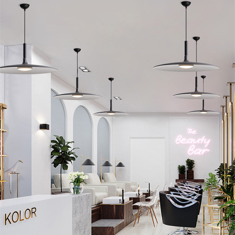 Separate dark disc pendants on ceiling canopies above seating and reception in a beauty salon