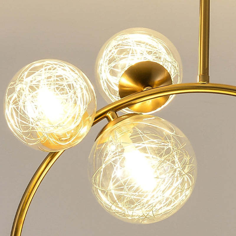 Close-up of clear globes with fine internal strands and gold-tone cups on a curved arm