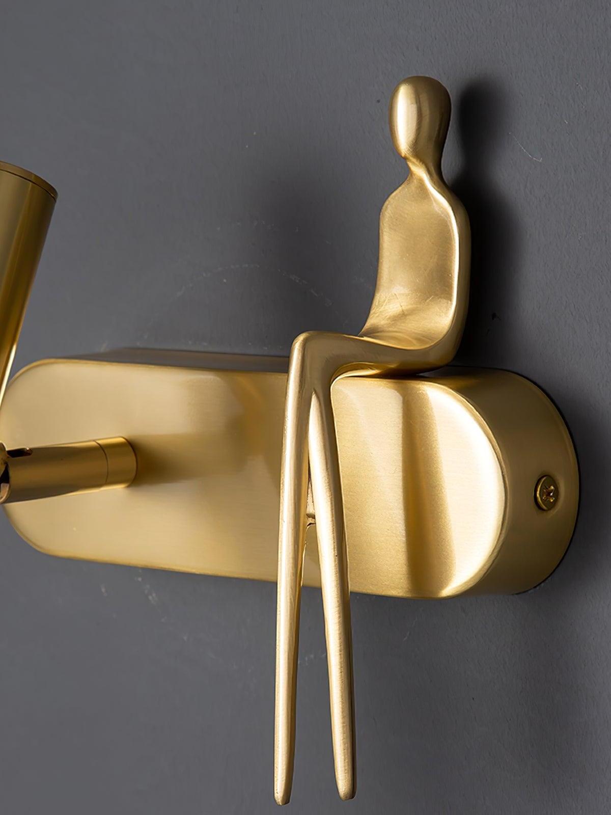 Close-up of gold-coloured seated figure with long legs on a rounded wallplate with a side fixing screw