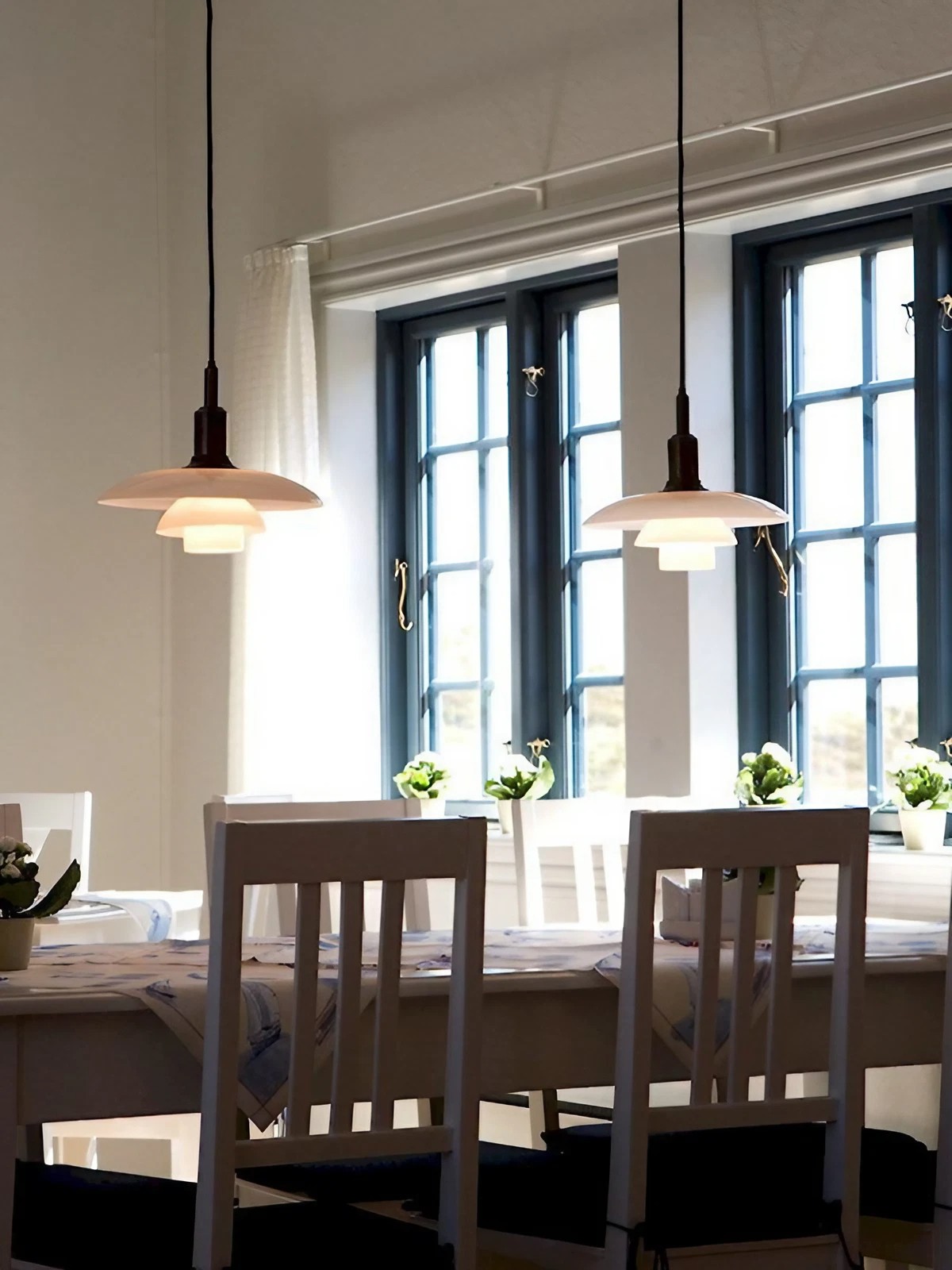 Two opal disc pendants above a dining table beside windows