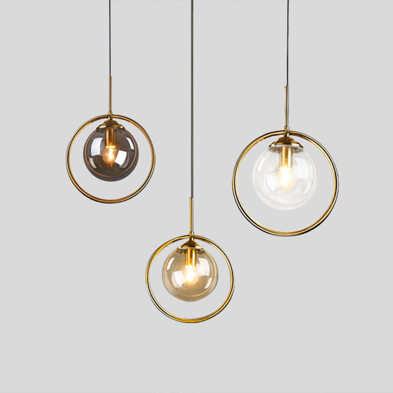Three separate Hailie pendants with gray, clear and cognac glass globes in gold-tone rings at different heights