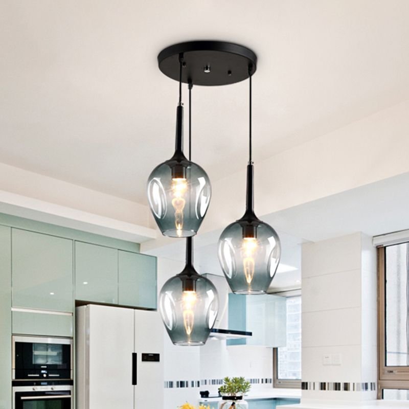 Blue glass cluster pendant with three shades above kitchen cabinets beside a window