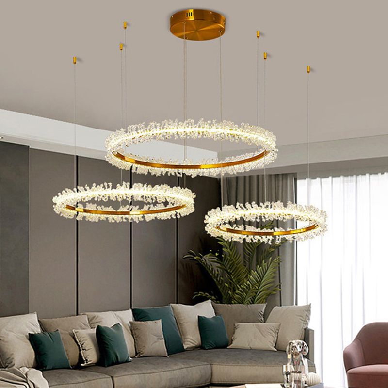 Round gold-tone canopy and three Kristy flower rings above grey seating and green cushions beside a white curtain.