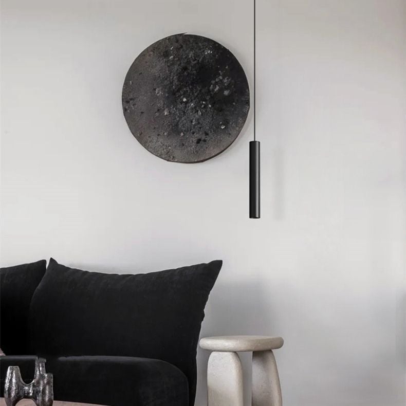 Black Edge cylinder pendant light near a dark sofa and round wall decoration