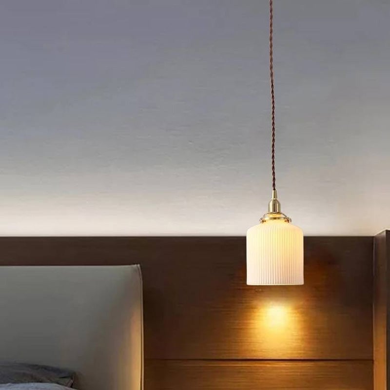 White cylindrical Valentina pendant illuminating a wooden headboard