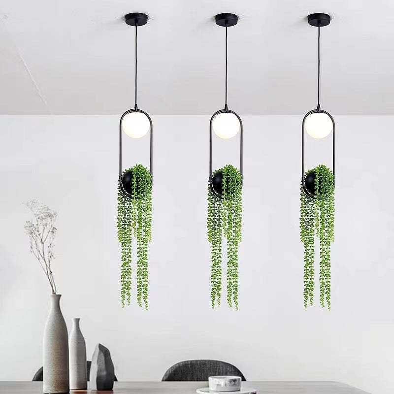 Three plant-decorated globe pendants above a dining table with vases and a cup against grey walls