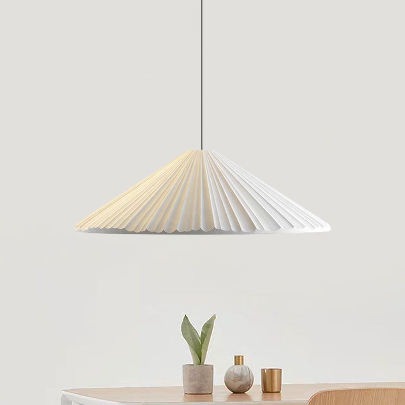 White shallow pleated cone pendant above a wooden table with a potted plant and gold-coloured vessels