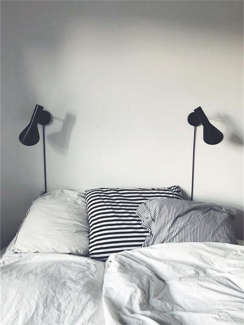 Two black Calix wall lamps pictured at the sides of a bed