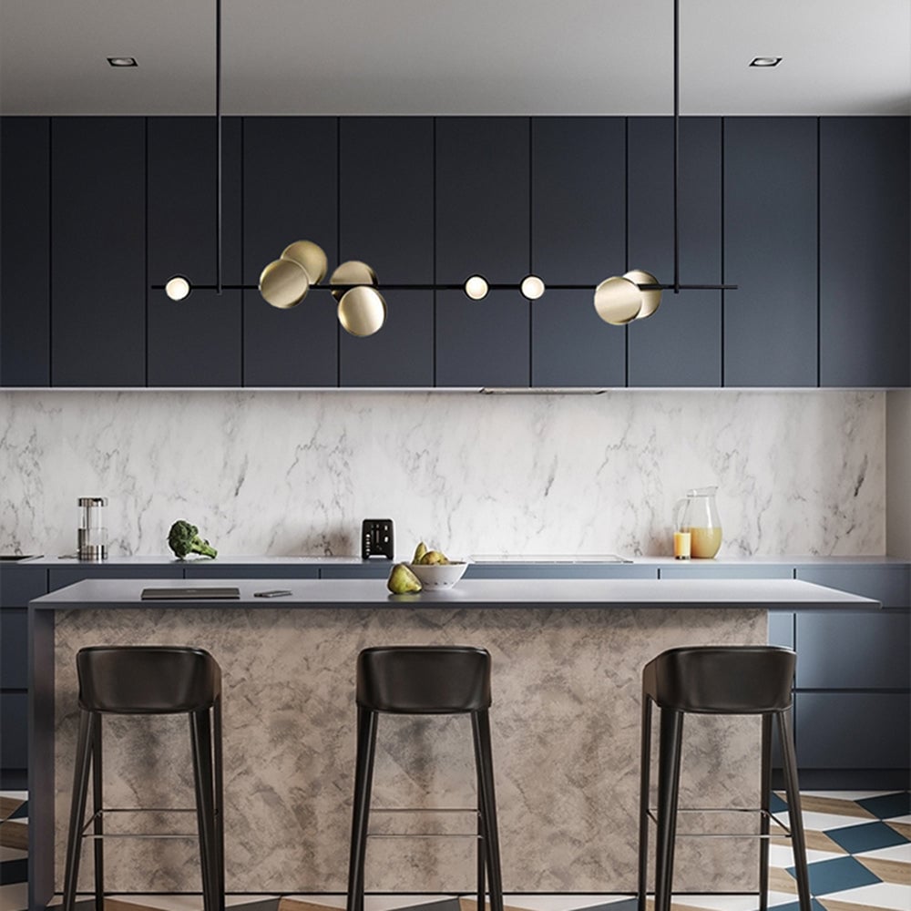 Avi black linear pendant with gold-tone discs above a kitchen island with dark stools and marble-pattern surfaces