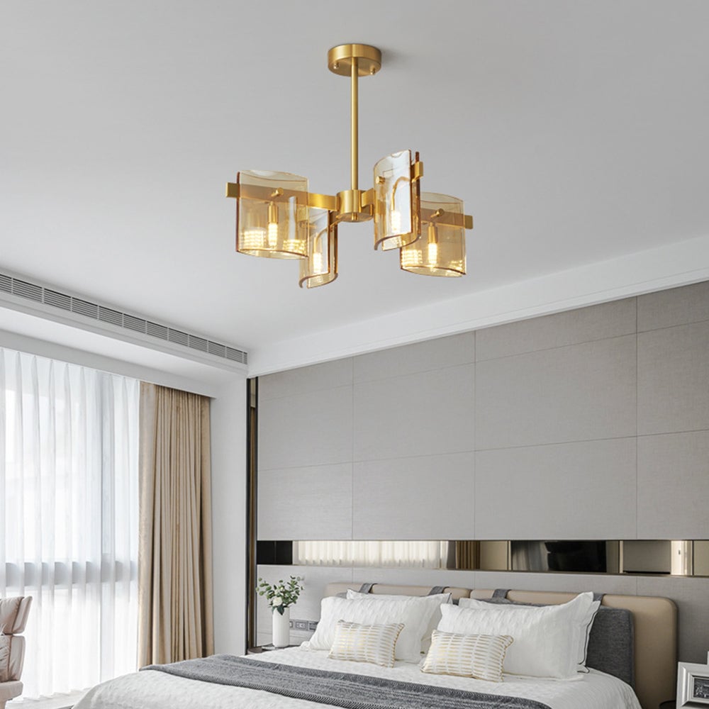 Gold 4-head pendant with amber-toned glass above a bed with white-grey pillows, pale headboard and curtains