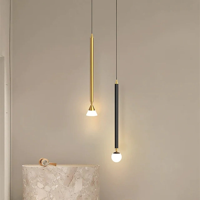 Gold cone-tip and black globe-tip Carr rod pendants at different heights above a rounded marble-look counter with a watch