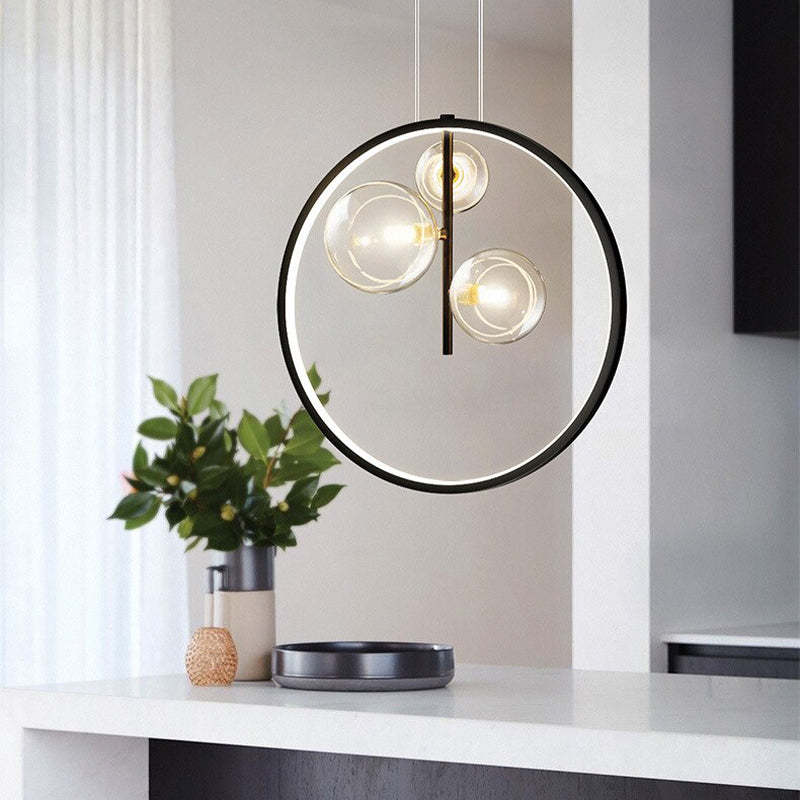 Three-globe black ring pendant above a white console with a black tray and leafy vase
