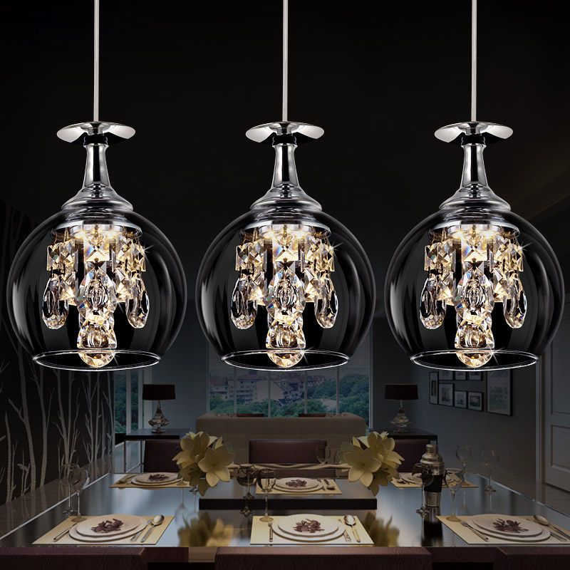 Three rounded Kristy clear glass pendant lights with faceted drops above a dining table against a dark background.