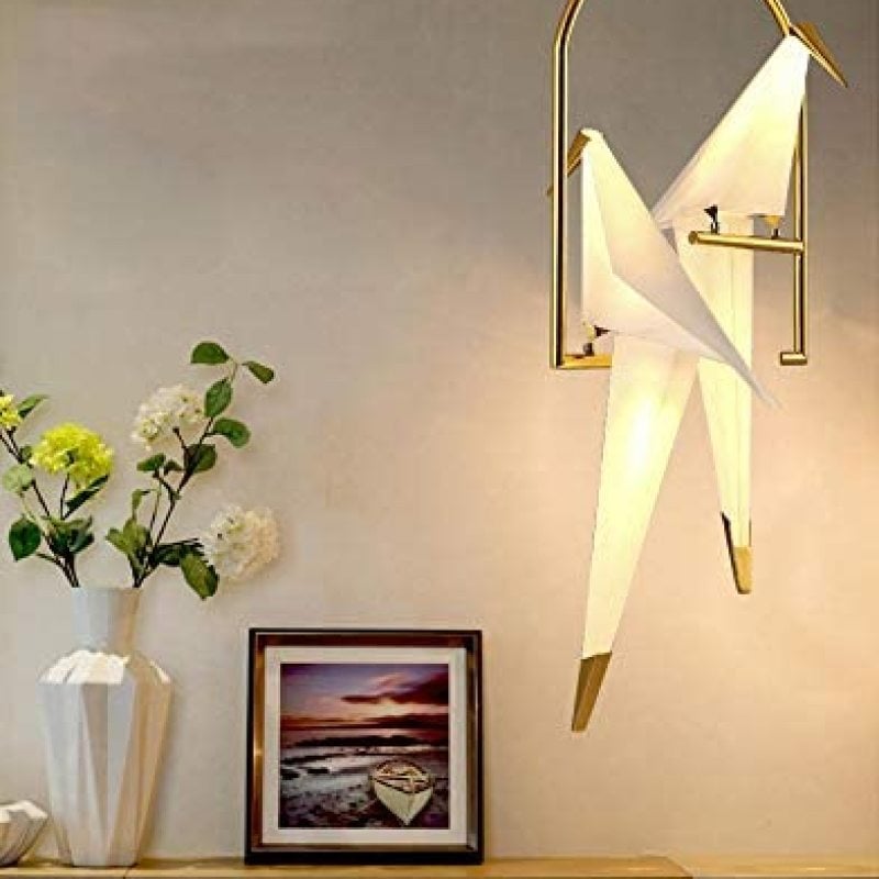 Two-bird pendant beside a framed picture and flowers on a side table.