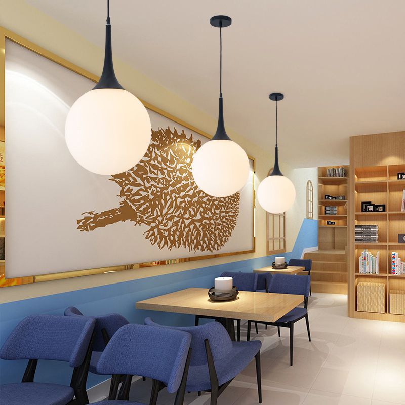 Three white Valentina globe pendants above wooden tables and blue seating, with gold leaf wall art and bookshelf