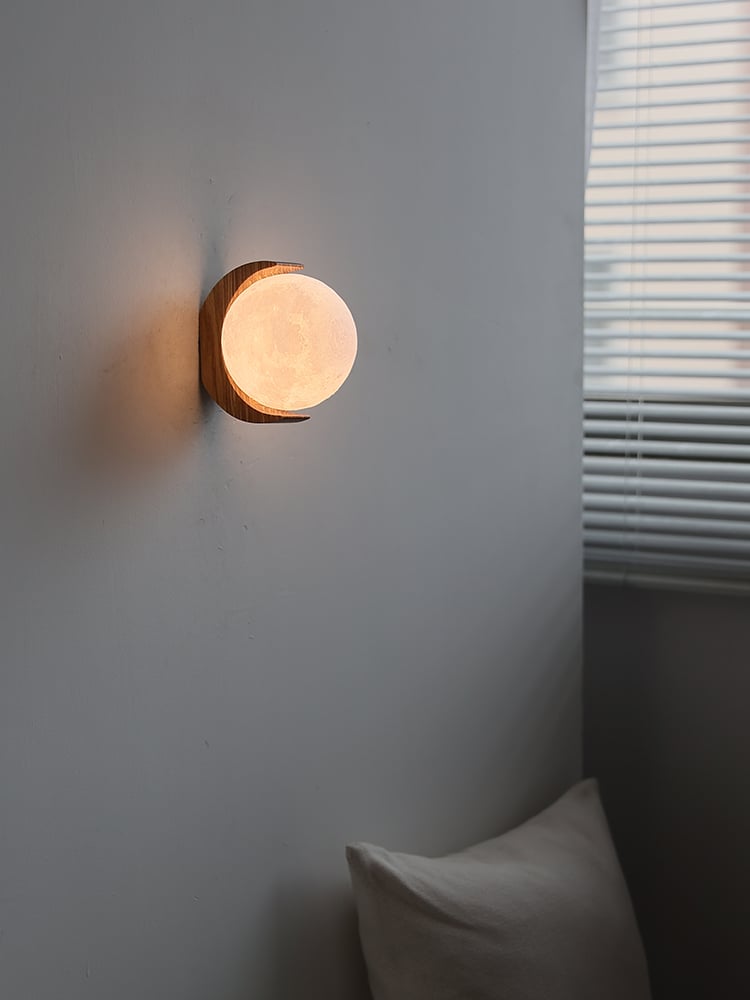 Moon globe wall light above two pale cushions beside horizontal window blinds