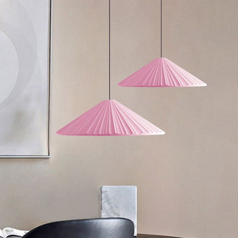 Two pink shallow pleated pendants at different heights above a table and black chair
