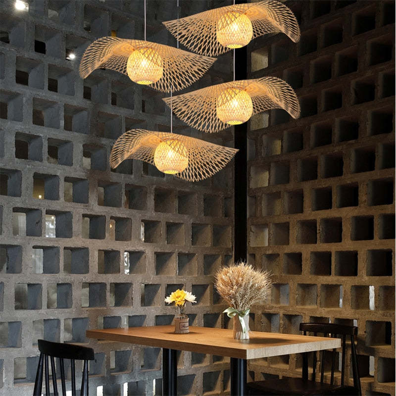Four basket-centred woven pendants above a wood table with black chairs against hollow-block walls