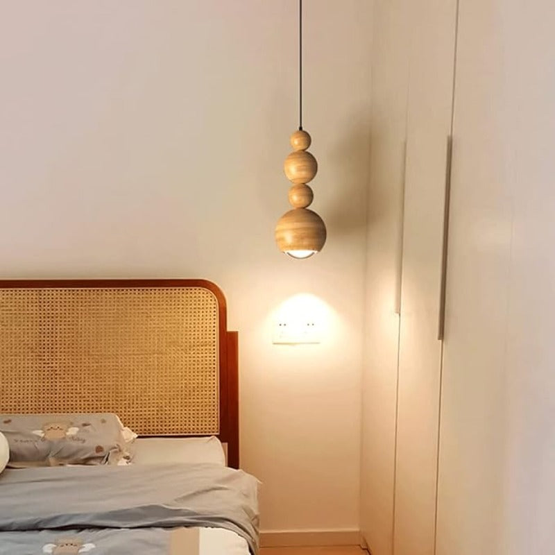 Wood-coloured Muto stacked-sphere pendant illuminated beside a bed.