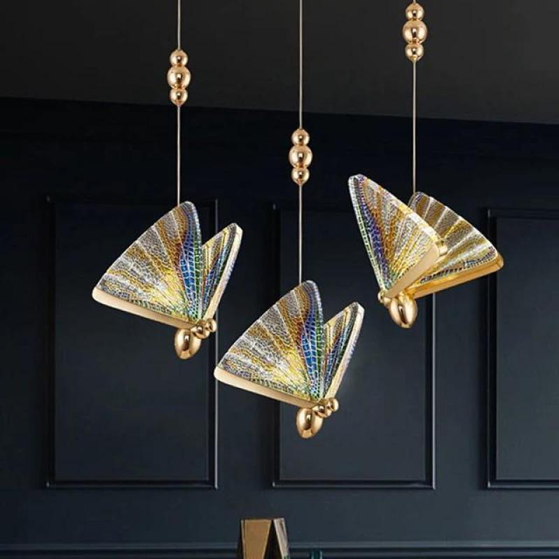 Three iridescent Kady butterfly pendants against a dark wall