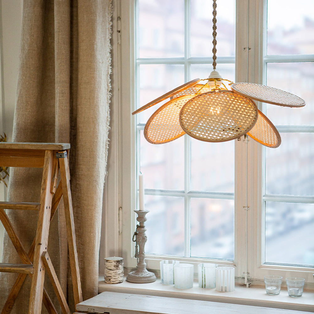 Lit woven petal pendant by a window and brown curtains above a table with candles and glasses
