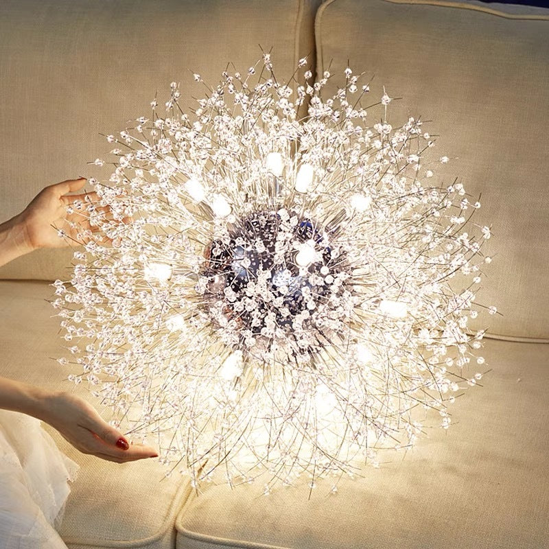 Chrome Lili with reflective silver-tone centre, lit lamps and clear clusters on fine stems, held at sides before beige sofa