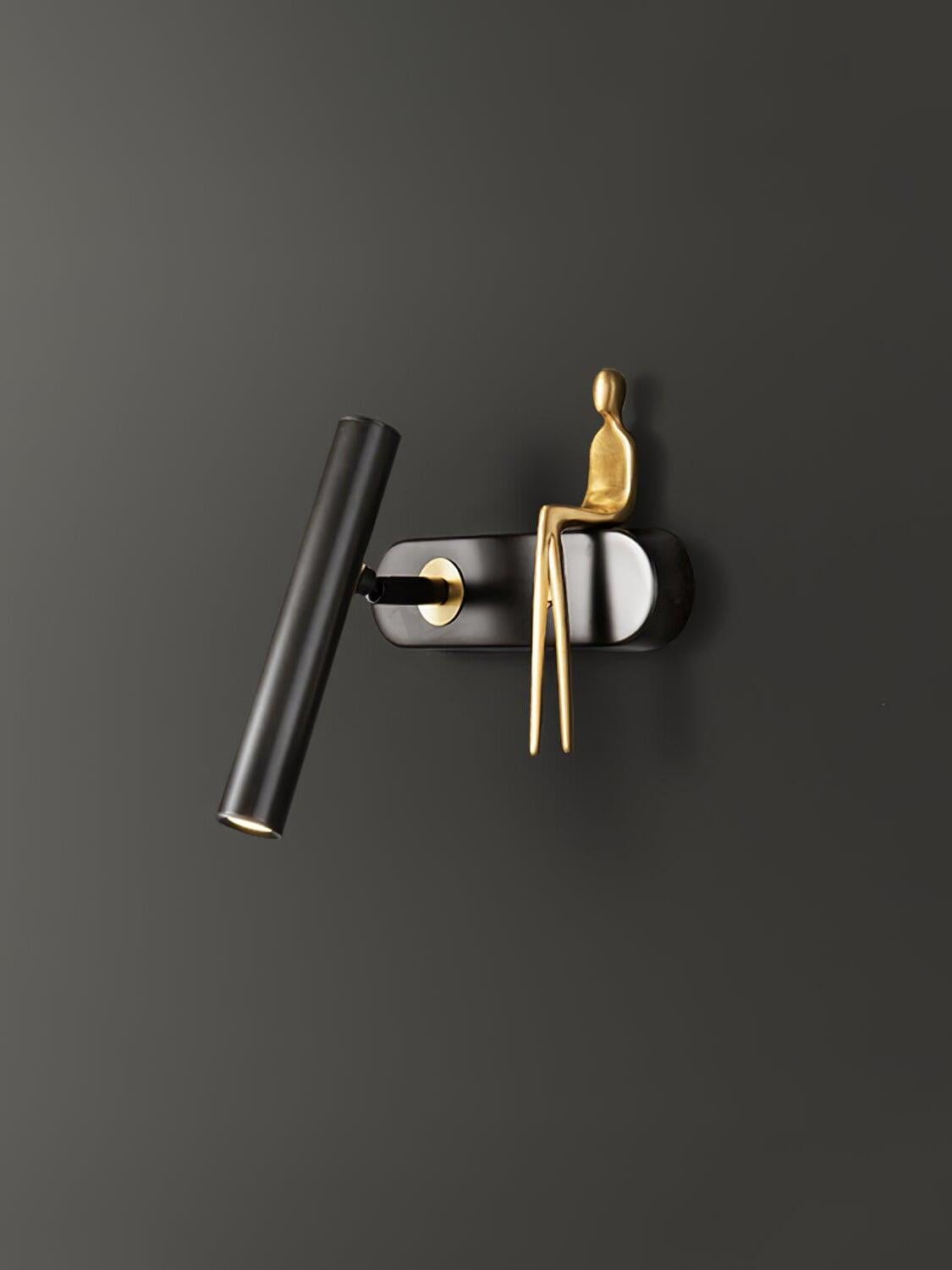 Angled close-up of black tube and wallplate with a gold-coloured seated figure and long dangling legs