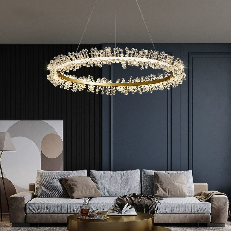 Single illuminated Kristy flower ring above a grey sofa and round gold-tone table against a dark panelled wall.