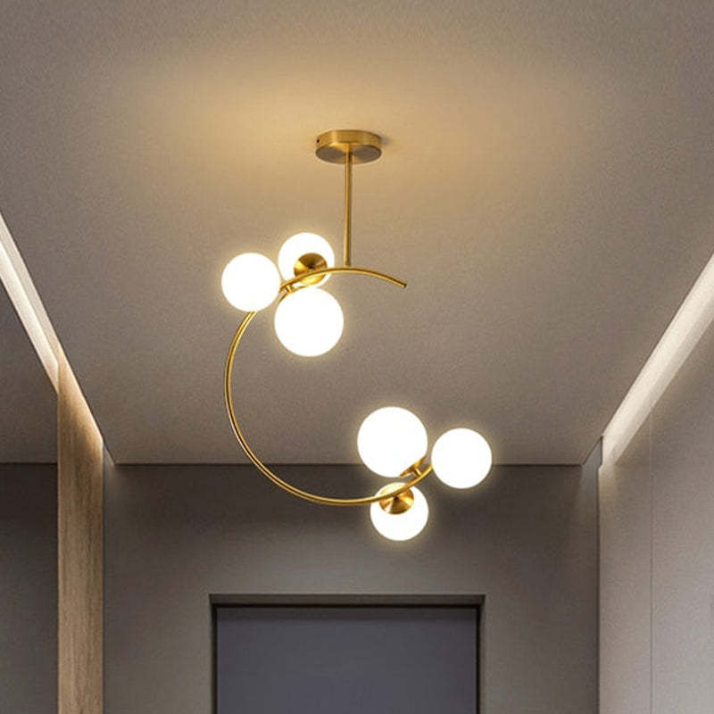 Front view of six white globes in upper and lower groups on a curved gold-tone ceiling light