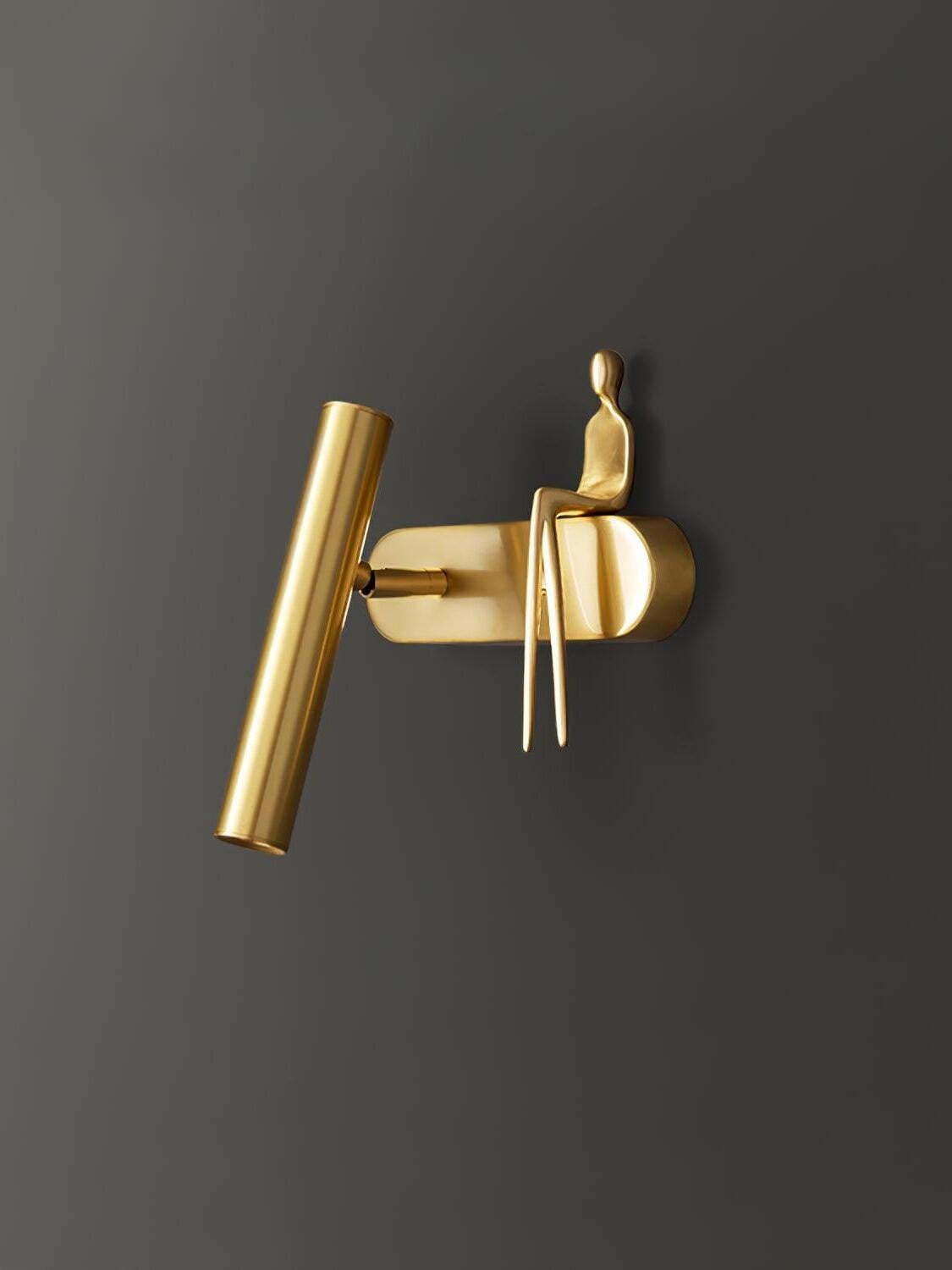 Angled close-up of brass-coloured tube, capsule-ended wallplate and seated figure