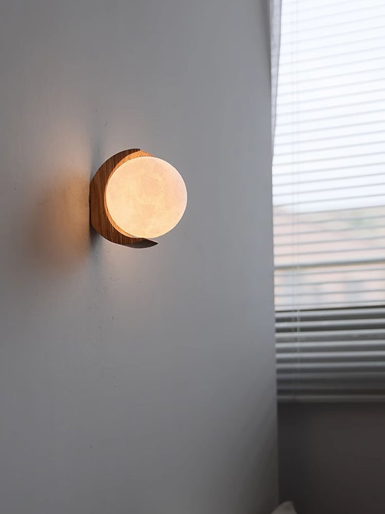 Angled view of a warm glowing moon globe framed by a wood crescent beside window blinds
