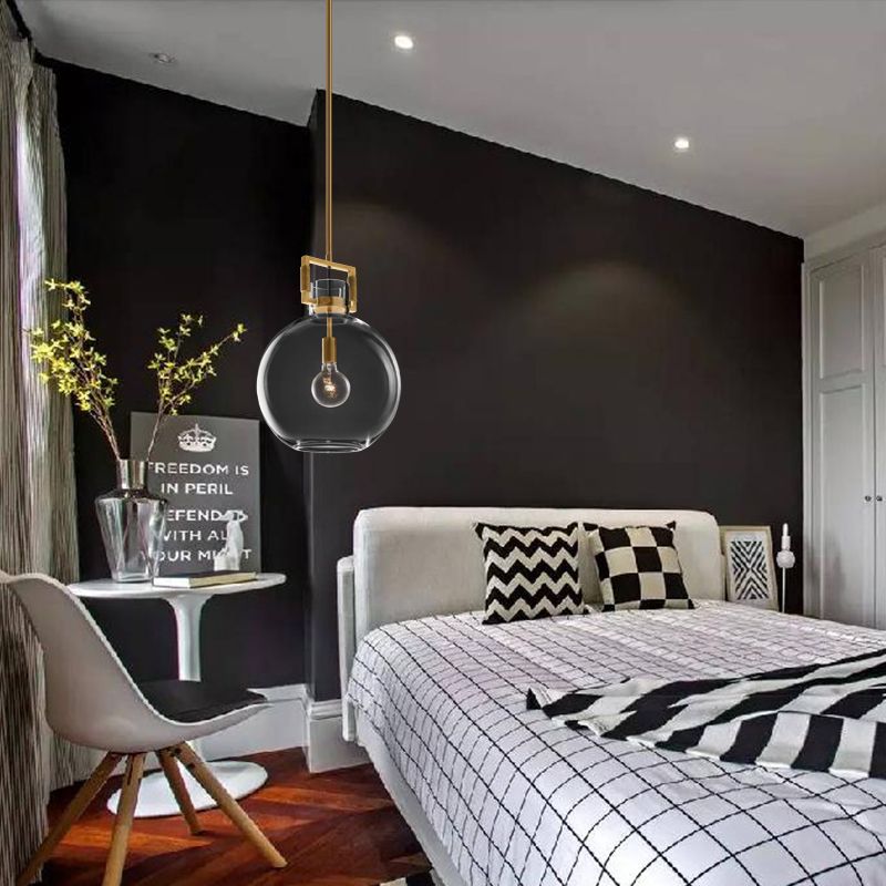 Cairns clear glass globe pendant beside a bed with black-and-white checked bedding and a branch vase